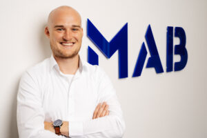 Lächelnder Mann in weißem Hemd vor Firmenwand mit verschränkten Armen